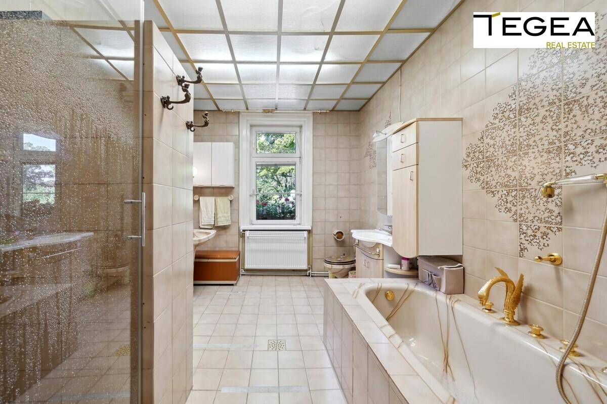 Geräumiges Badezimmer mit Badewanne, Dusche und Fenster, gefliest in beigen Farbtönen.