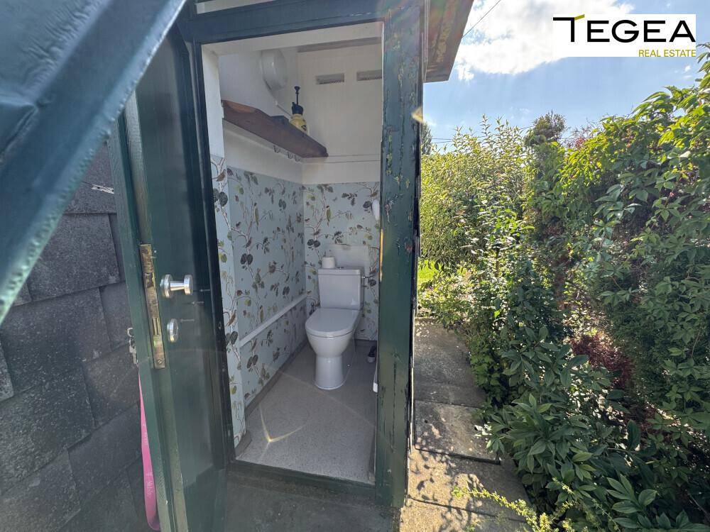 Kleines separates WC im Außenbereich mit einfacher Ausstattung und gemusterten Wänden.