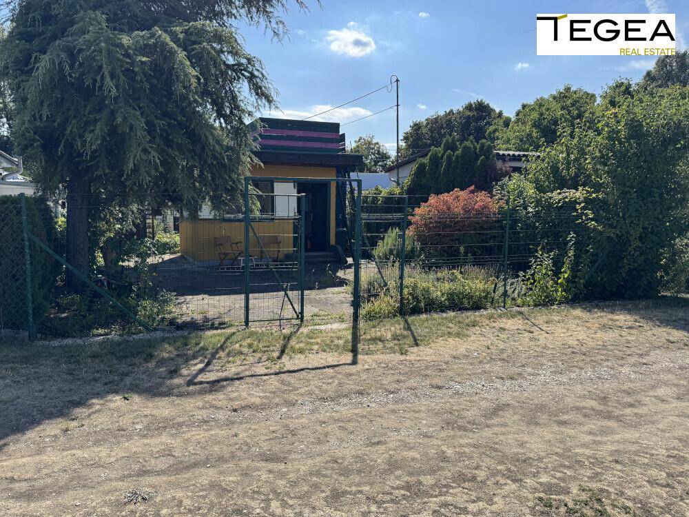 Kleines gelbes Gebäude mit Zaun und Bäumen in einer ländlichen Umgebung.