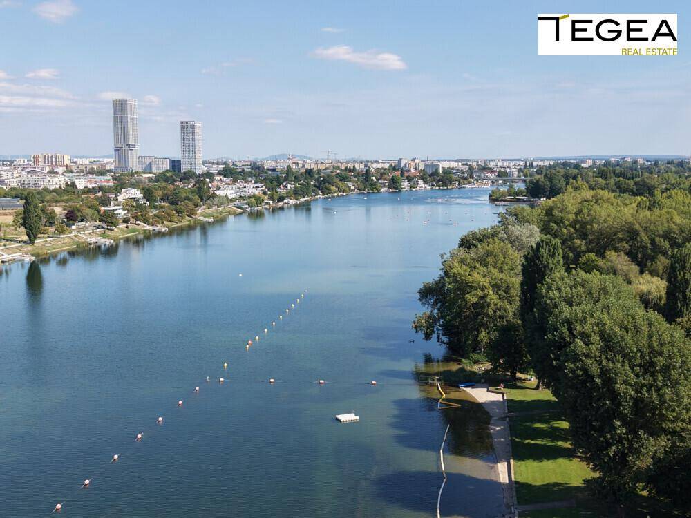 Luftaufnahme des breiten Flusses mit Badebereich und der Stadtkulisse am Horizont.