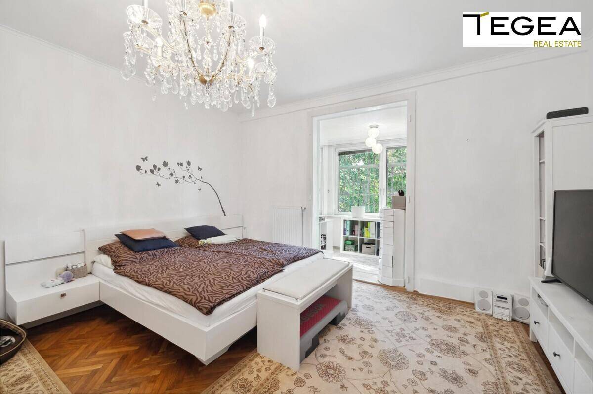Helles Schlafzimmer mit Doppelbett, Parkettboden und Kronleuchter, mit Zugang zu einem weiteren Raum.