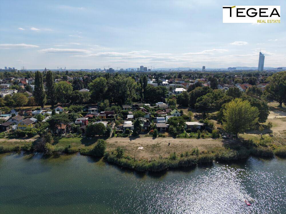 Luftaufnahme des Sees mit Uferbebauung und der Skyline im Hintergrund.