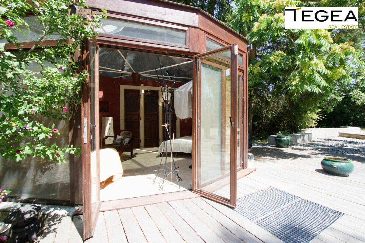Ein charmantes Gartenhaus oder Wintergarten mit großen Glastüren, die sich zu einer Holzterrasse öffnen.