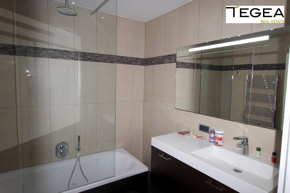 Badezimmer mit Badewanne, Waschtisch und Spiegelschrank in hellen Fliesen.