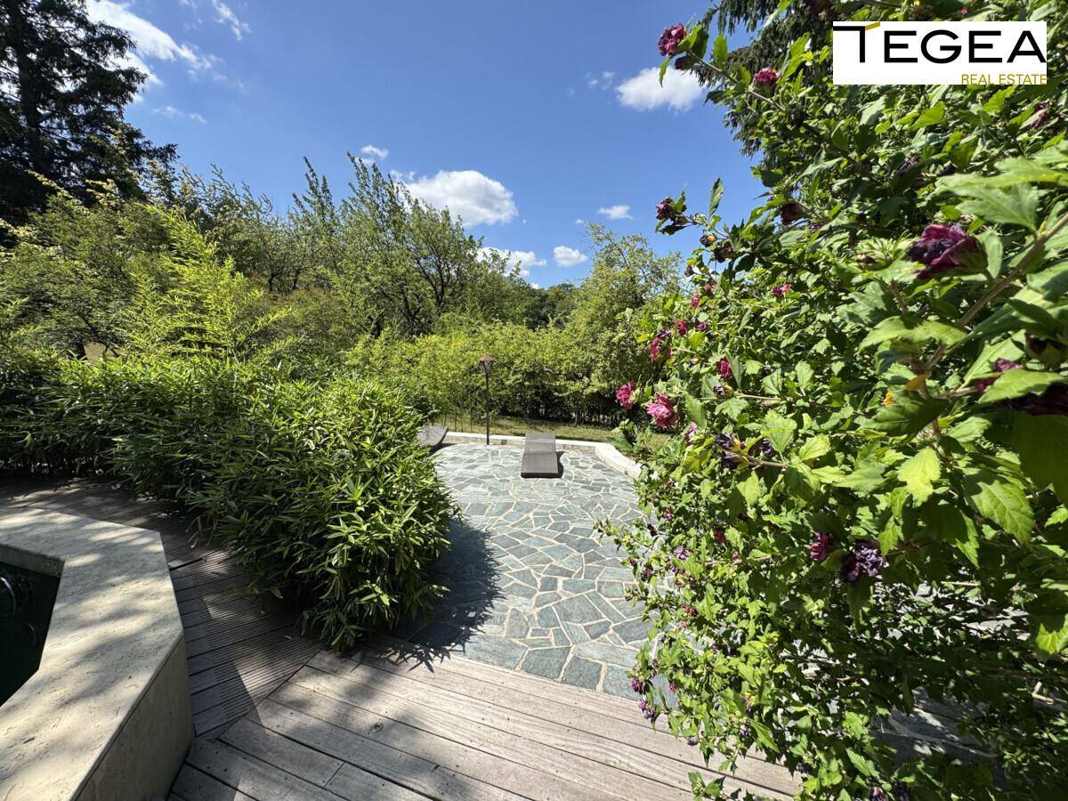 Gepflasterter Gartenbereich mit Holzdeck und üppiger Bepflanzung, ideal zum Entspannen im Freien.