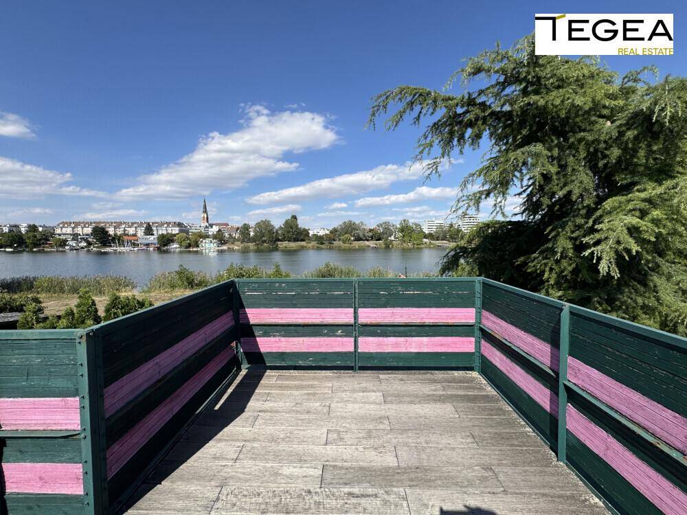 Holzbalkon mit Blick auf den See und die gegenüberliegende Uferbebauung.