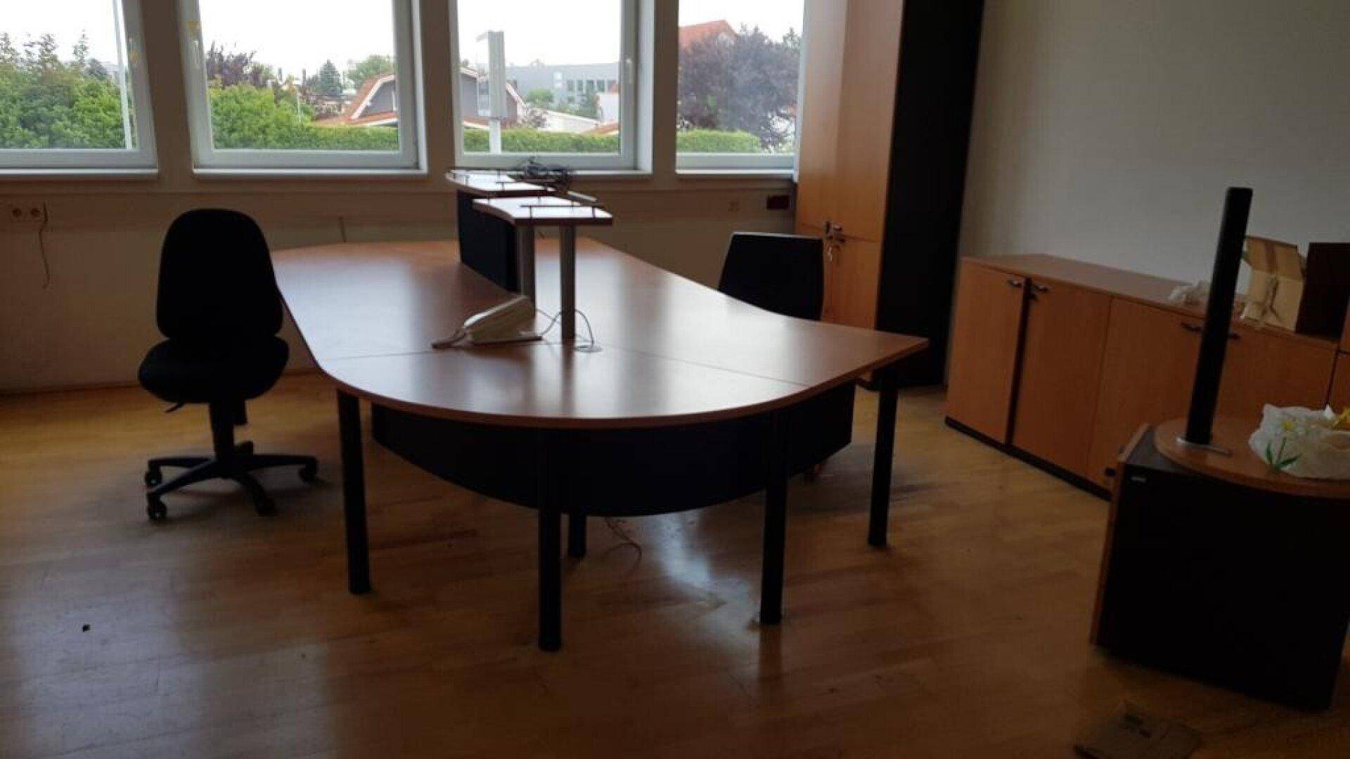 Geräumiges Büro mit Holzfußboden, großem Schreibtisch und Blick ins Grüne.