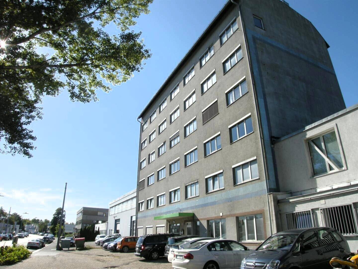 Mehrstöckiges Geschäftsgebäude mit Parkplätzen und Bäumen unter blauem Himmel.