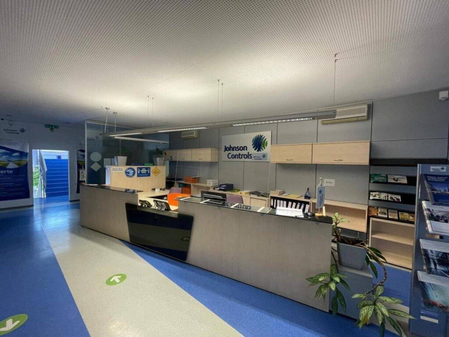 Empfangsbereich mit moderner Theke, blauer Bodenmarkierung und Firmenlogo an der Wand.