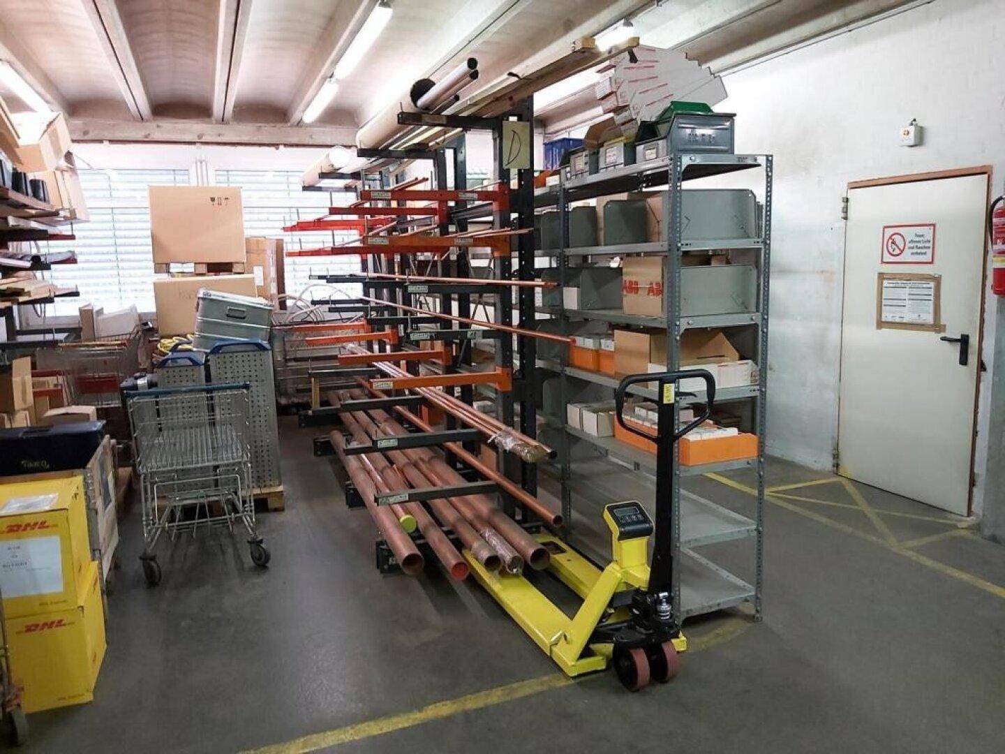Industrieller Lagerbereich mit hohen Regalen, Rohren und einem Hubwagen für Materialtransport.