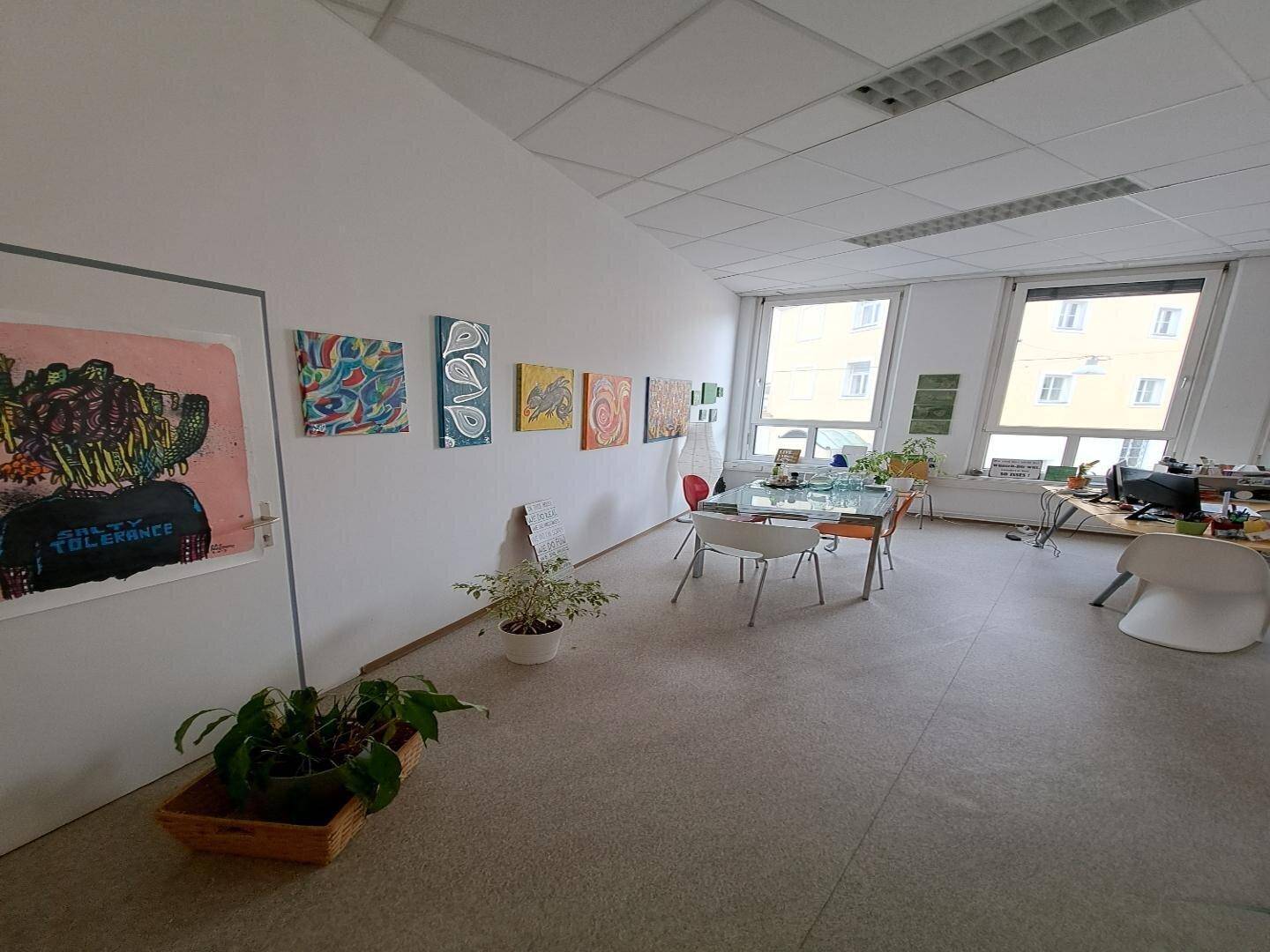 Geräumiges Büro mit Kunstwerken an den Wänden, großen Fenstern und einem flexiblen Besprechungsbereich.