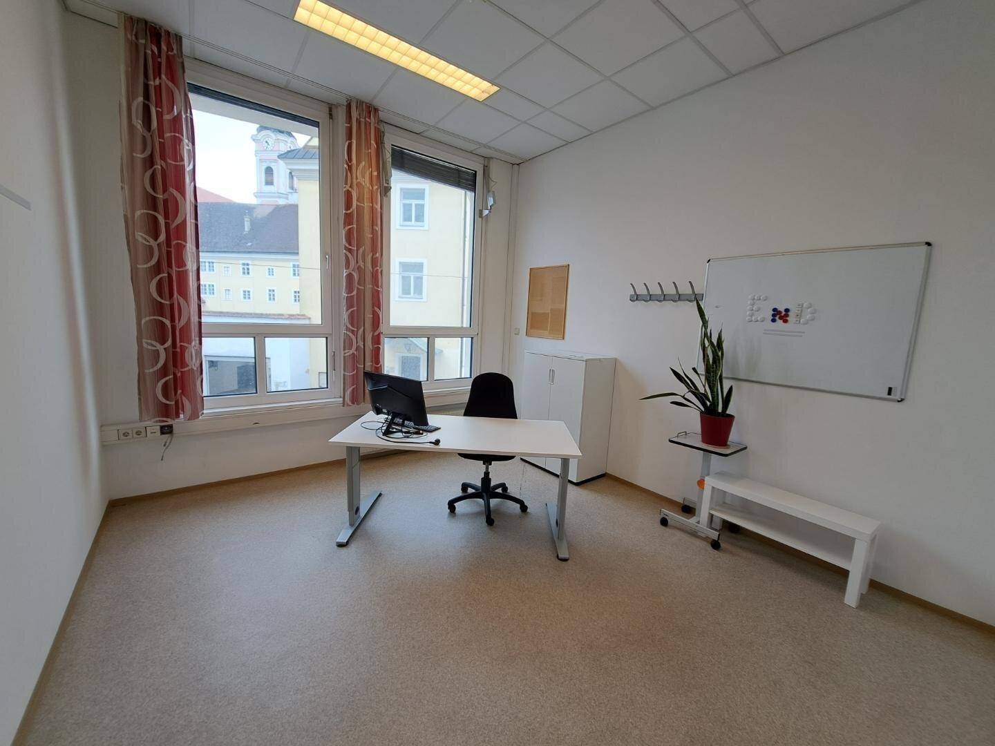 Helles Büro mit Schreibtisch, Stuhl, Whiteboard und Blick auf die Stadt durch die großen Fenster.