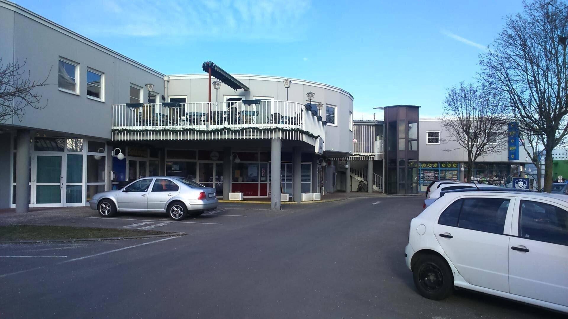 Außenansicht eines Geschäftsgebäudes mit Parkplatz und einer geschwungenen Fassade mit Balkon.