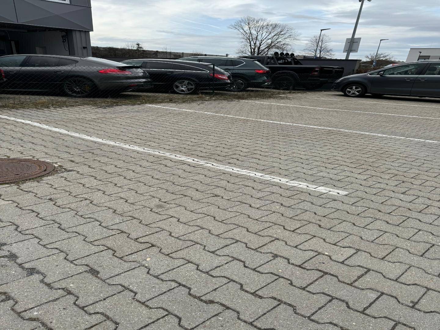 Nahaufnahme eines gepflasterten Parkplatzes mit mehreren Autos und einem Teil eines modernen Gebäudes im Hintergrund.