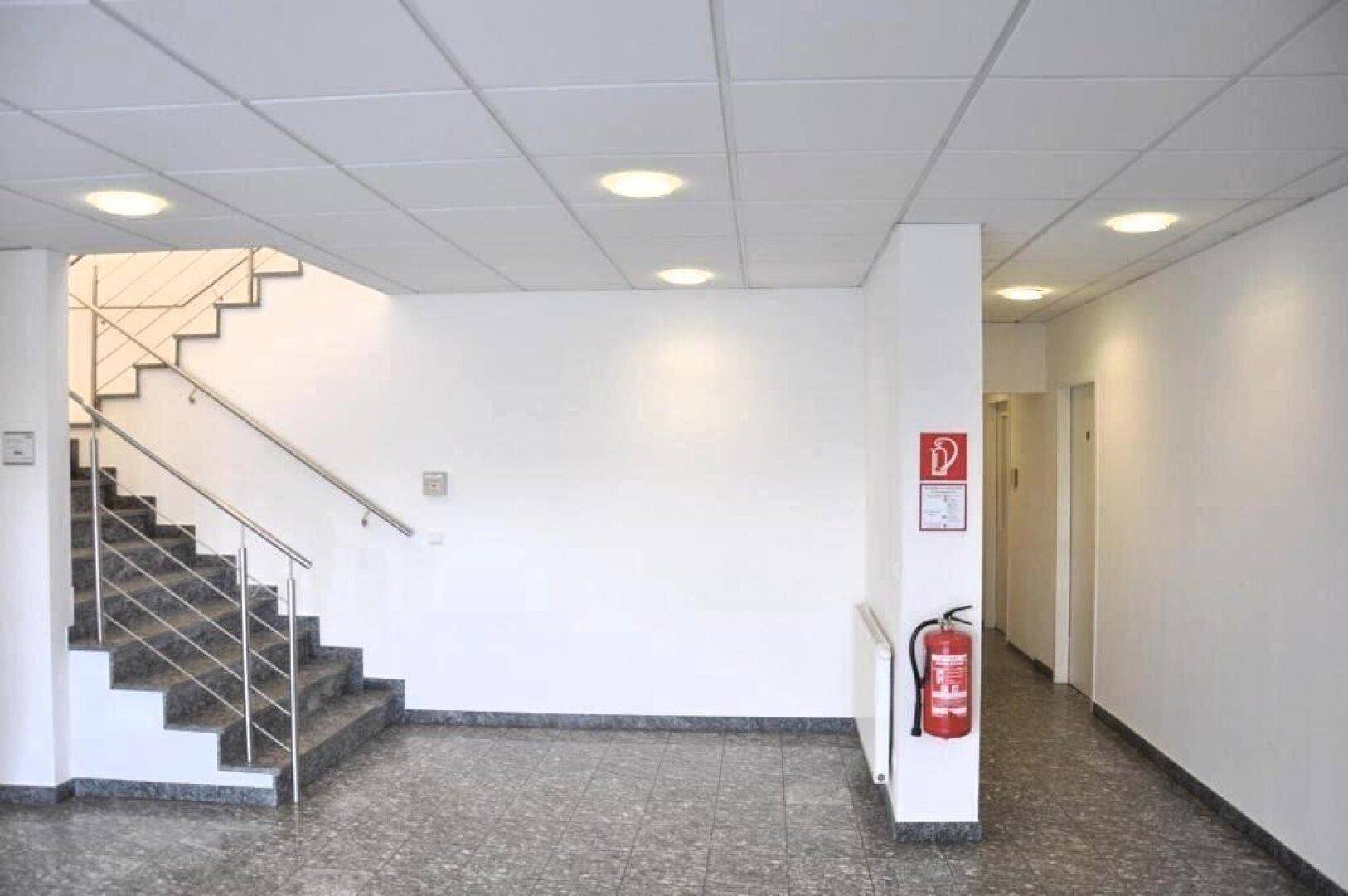 Heller Flur und Treppenhaus mit Granitboden, abgehängter Decke und eingelassenen Lichtern.