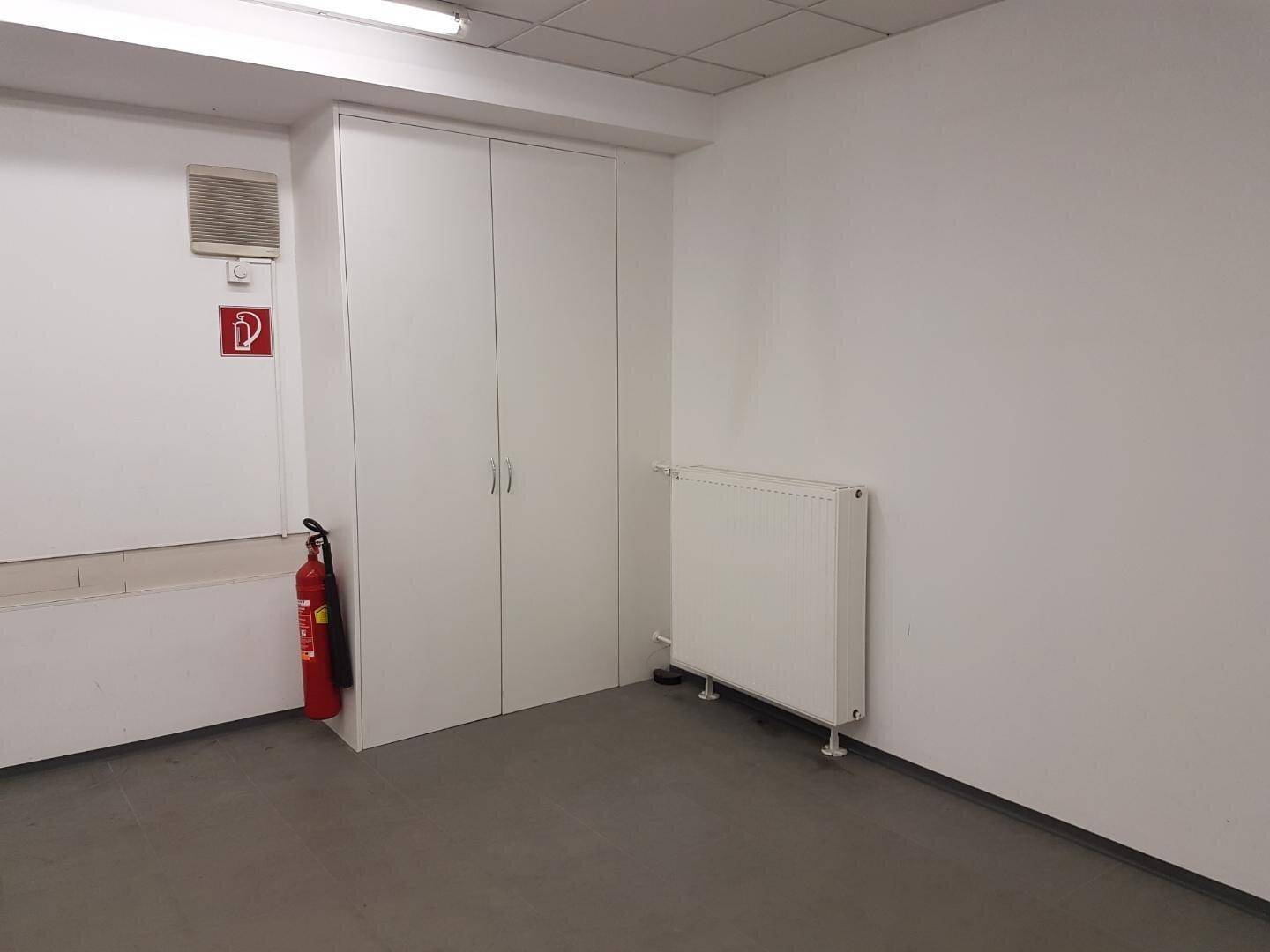 Detailansicht eines Gewerberaums mit weißem Einbauschrank, Heizkörper und Feuerlöscher an der Wand.
