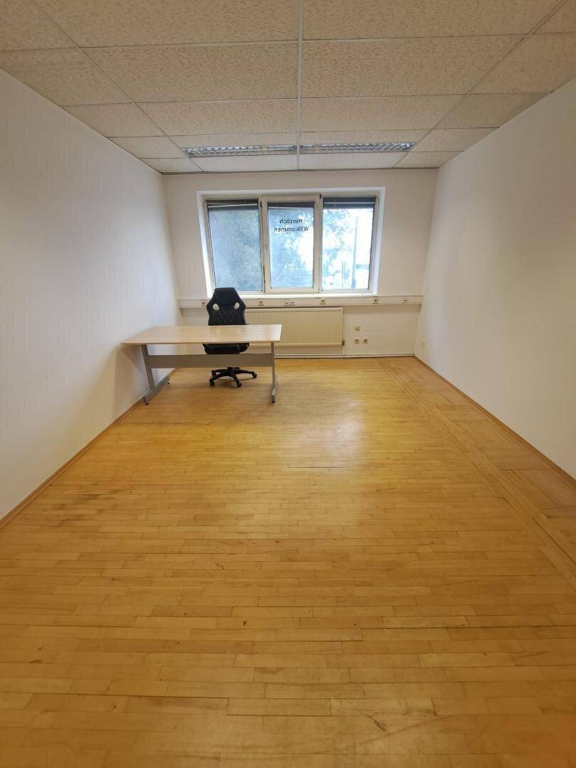Funktionaler Büroraum mit Schreibtisch, Bürostuhl und Blick nach draußen durch die Fenster.