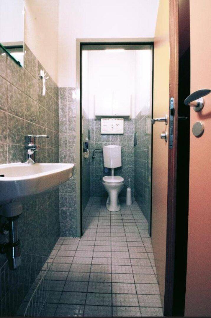 Kleiner Toilettenraum mit grauen Fliesen an Wänden und Boden, Waschbecken und WC.