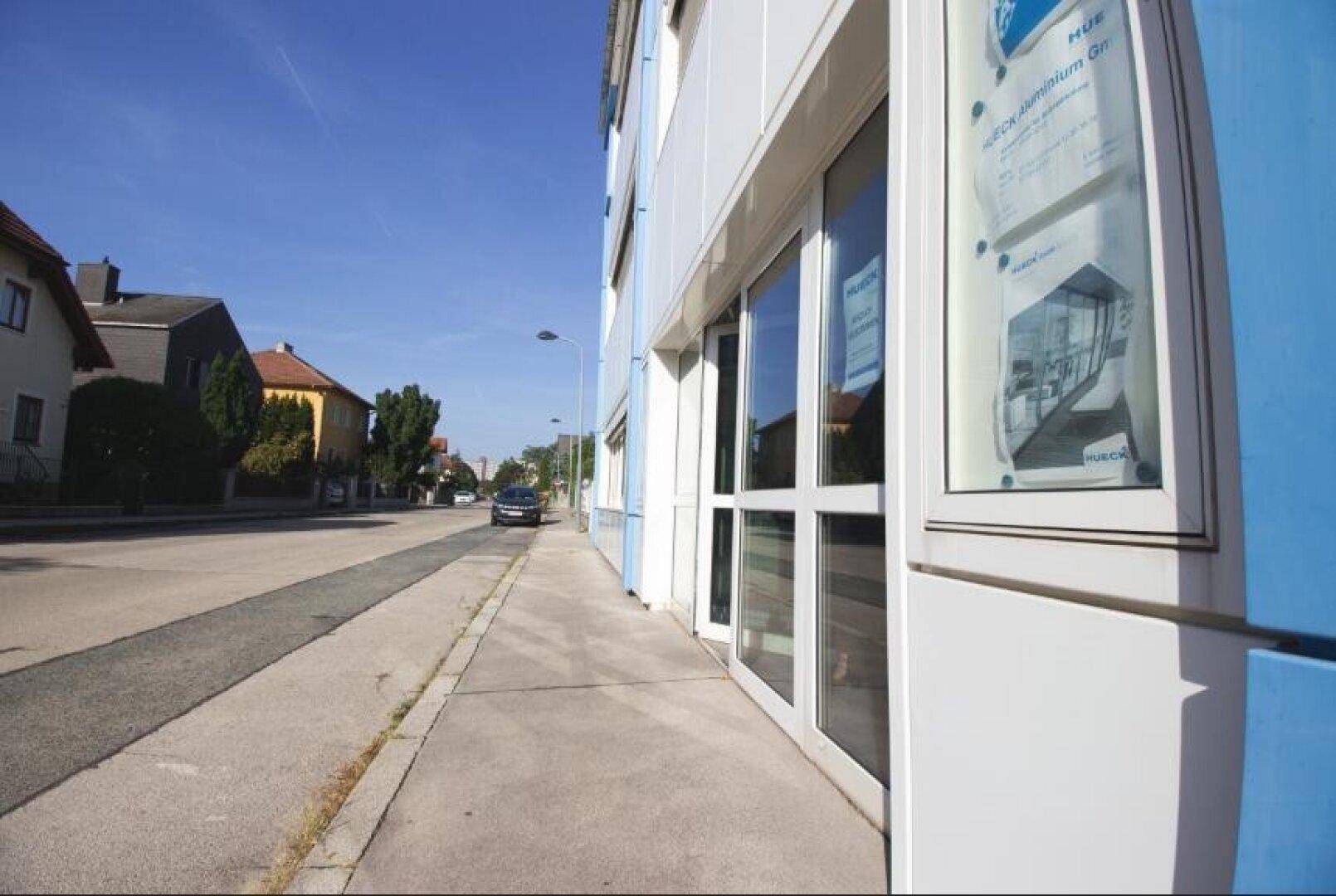 Außenansicht eines Gebäudes mit großen Fenstern und blauen Akzenten entlang einer Straße.