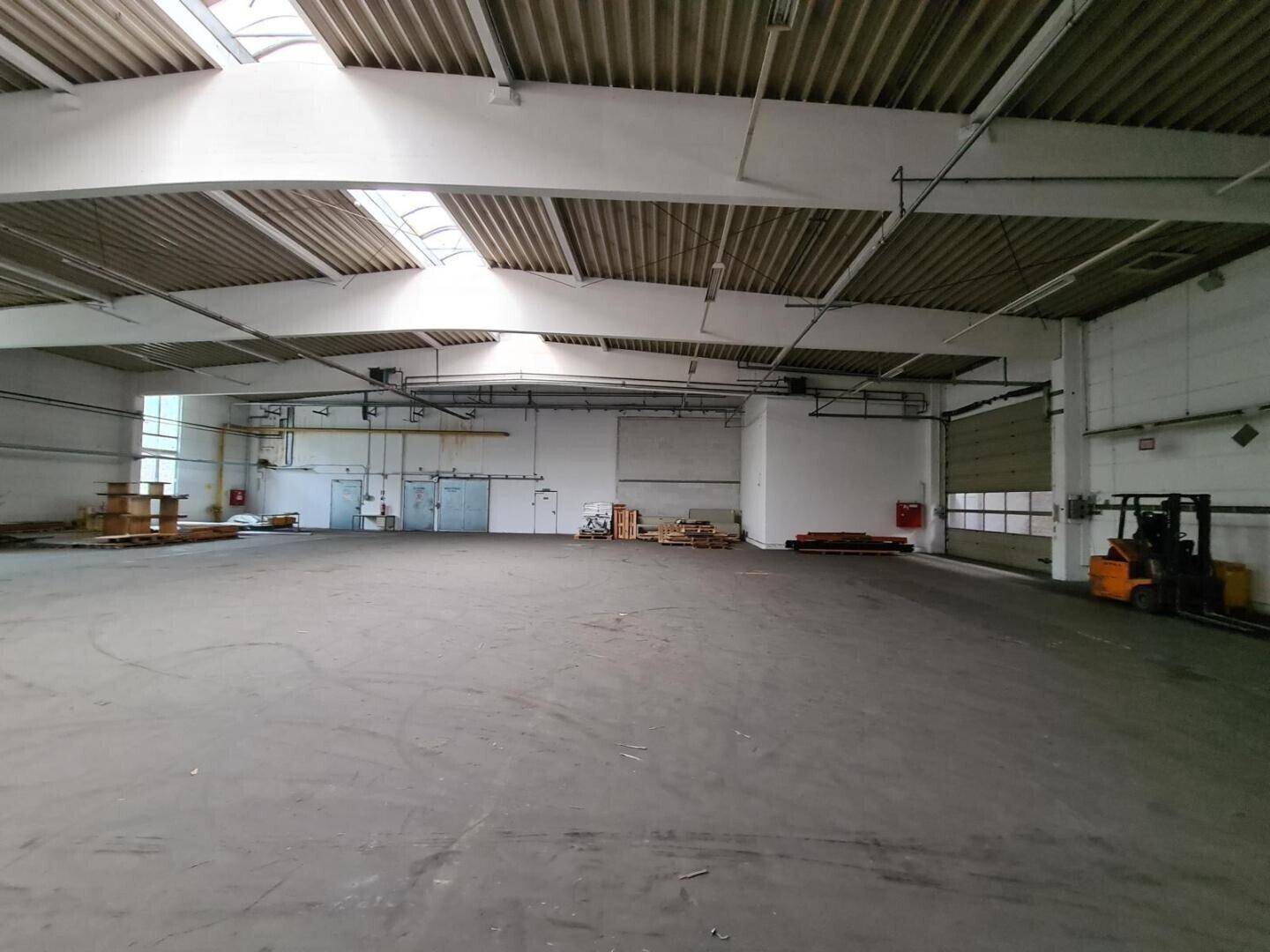 Weitläufige Lagerhalle mit Betonboden, hohen Decken und einem Rolltor für den Wareneingang.