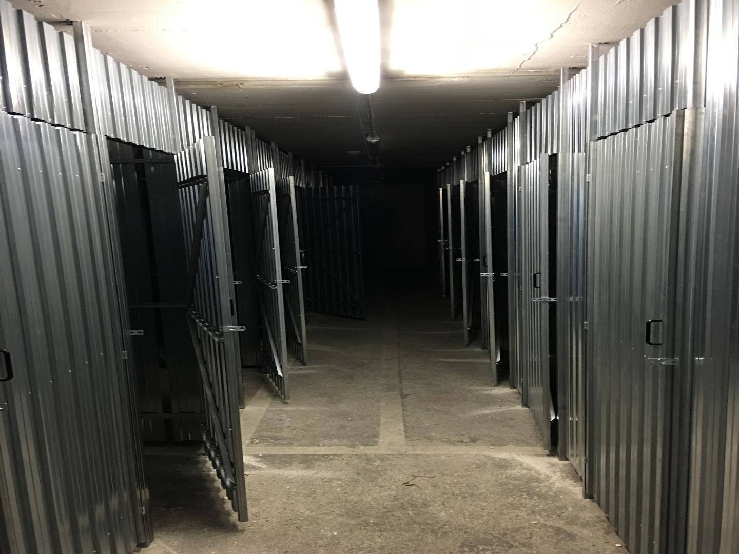 Hellerer Blick auf den Kellergang mit vielen individuellen Lagerabteilen aus Metall und Betonboden.