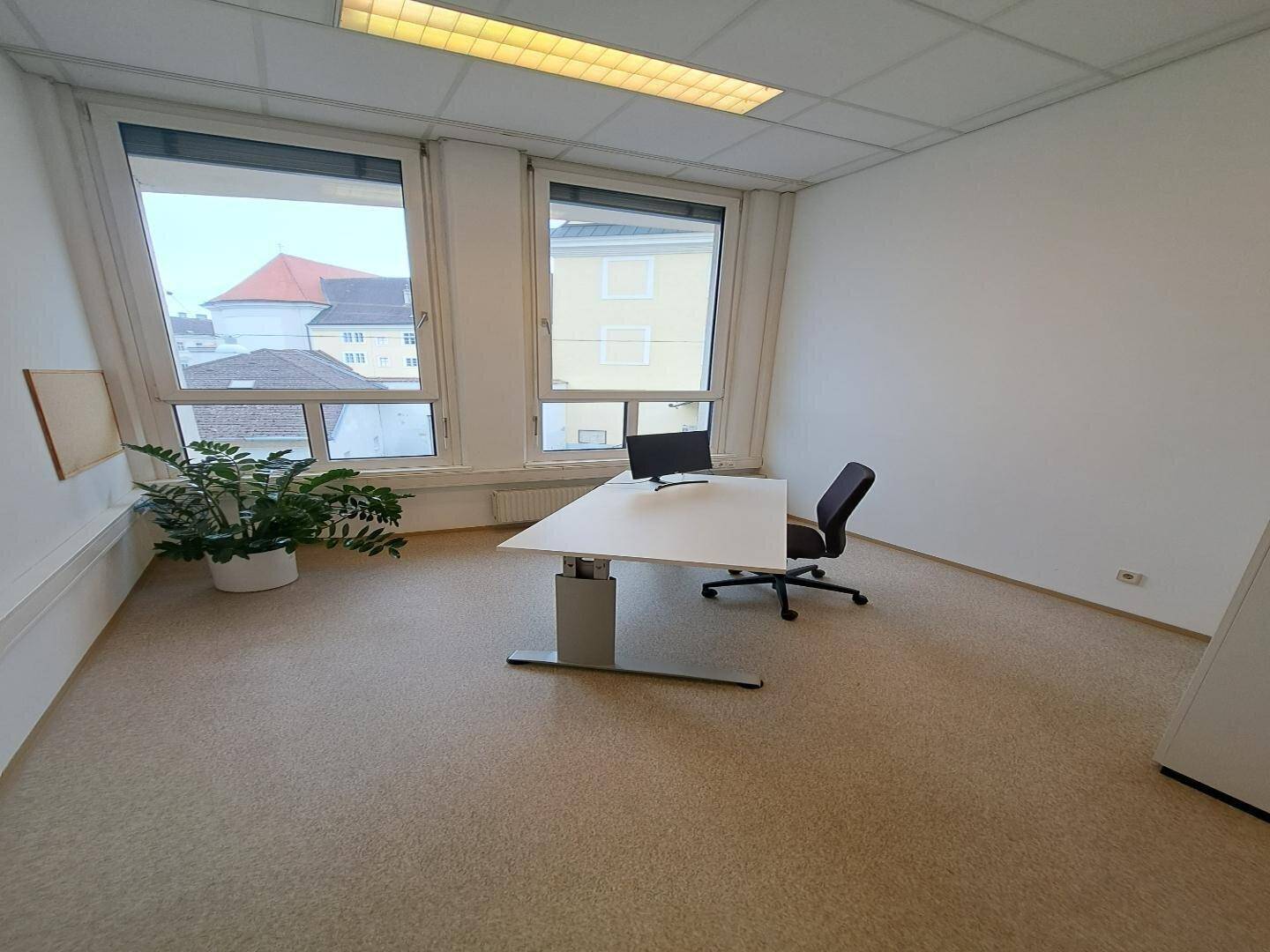 Helles Einzelbüro mit großem, höhenverstellbarem Schreibtisch und ergonomischem Stuhl, bietet eine ruhige Arbeitsumgebung.