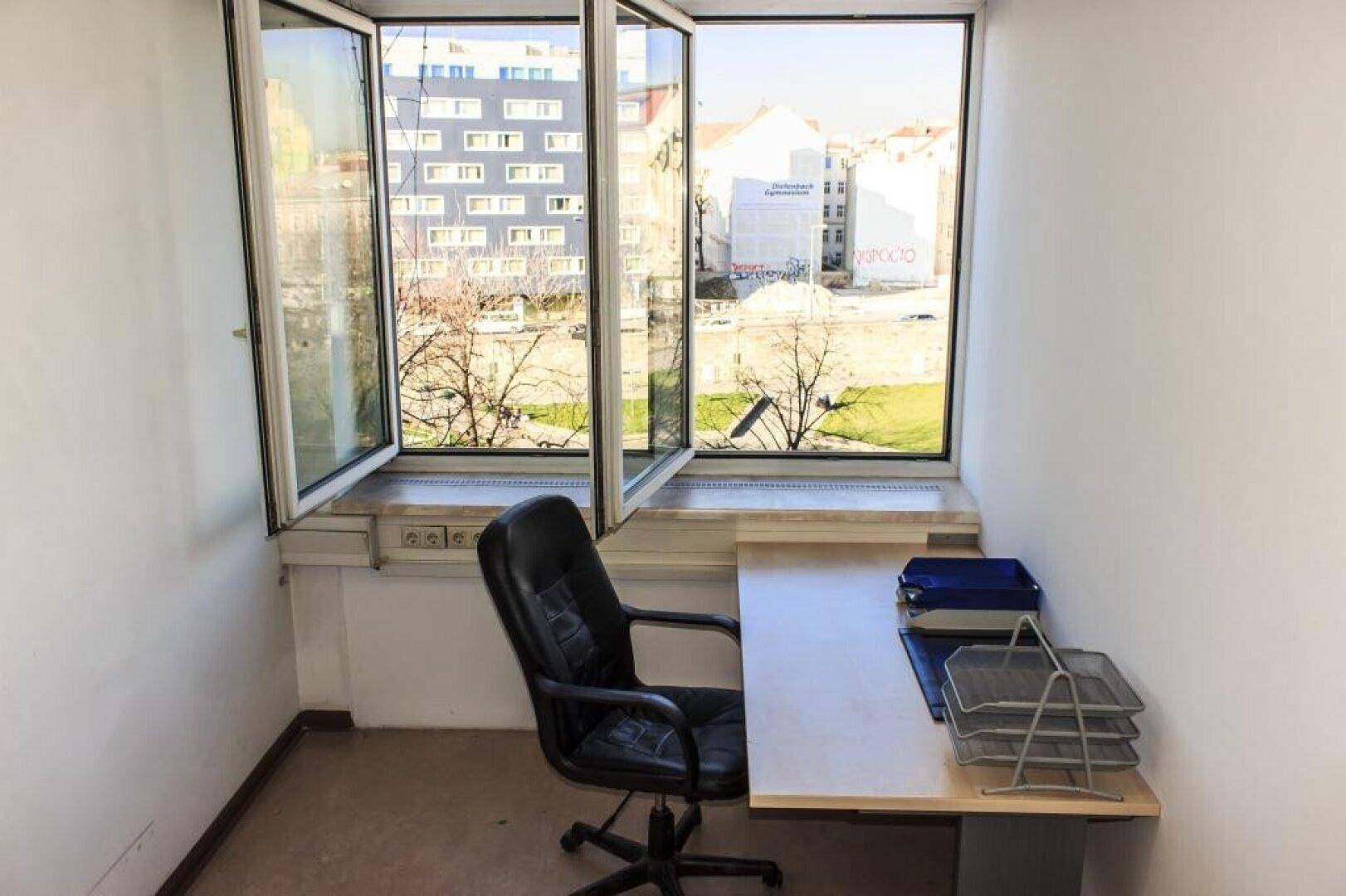 Kleines Büro mit Schreibtisch und Stuhl, hell durch ein großes Fenster mit Blick auf die Stadt.