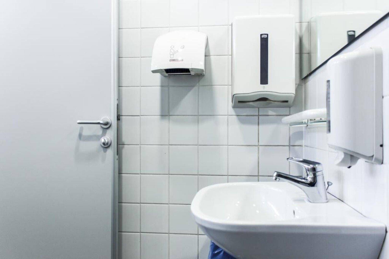 Badezimmer mit weiß gefliesten Wänden, Waschbecken und modernen Handtuchspendern.