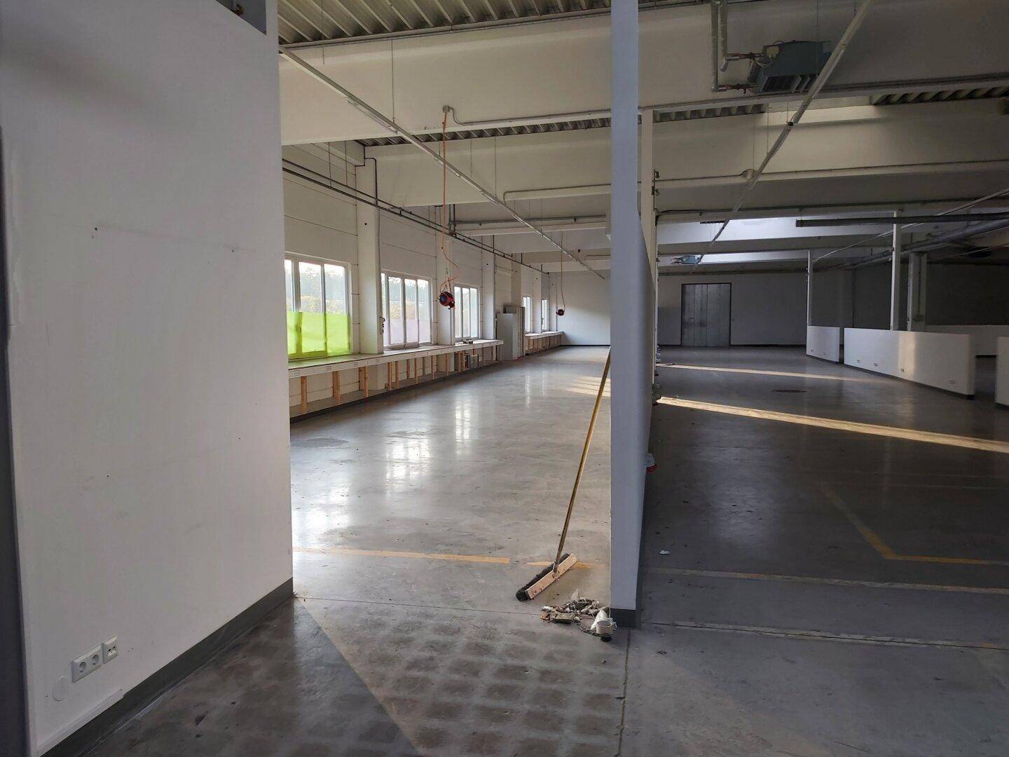 Langer Gangbereich im Industrieraum mit vielen Fenstern entlang einer Wand, die viel Tageslicht hereinlassen.
