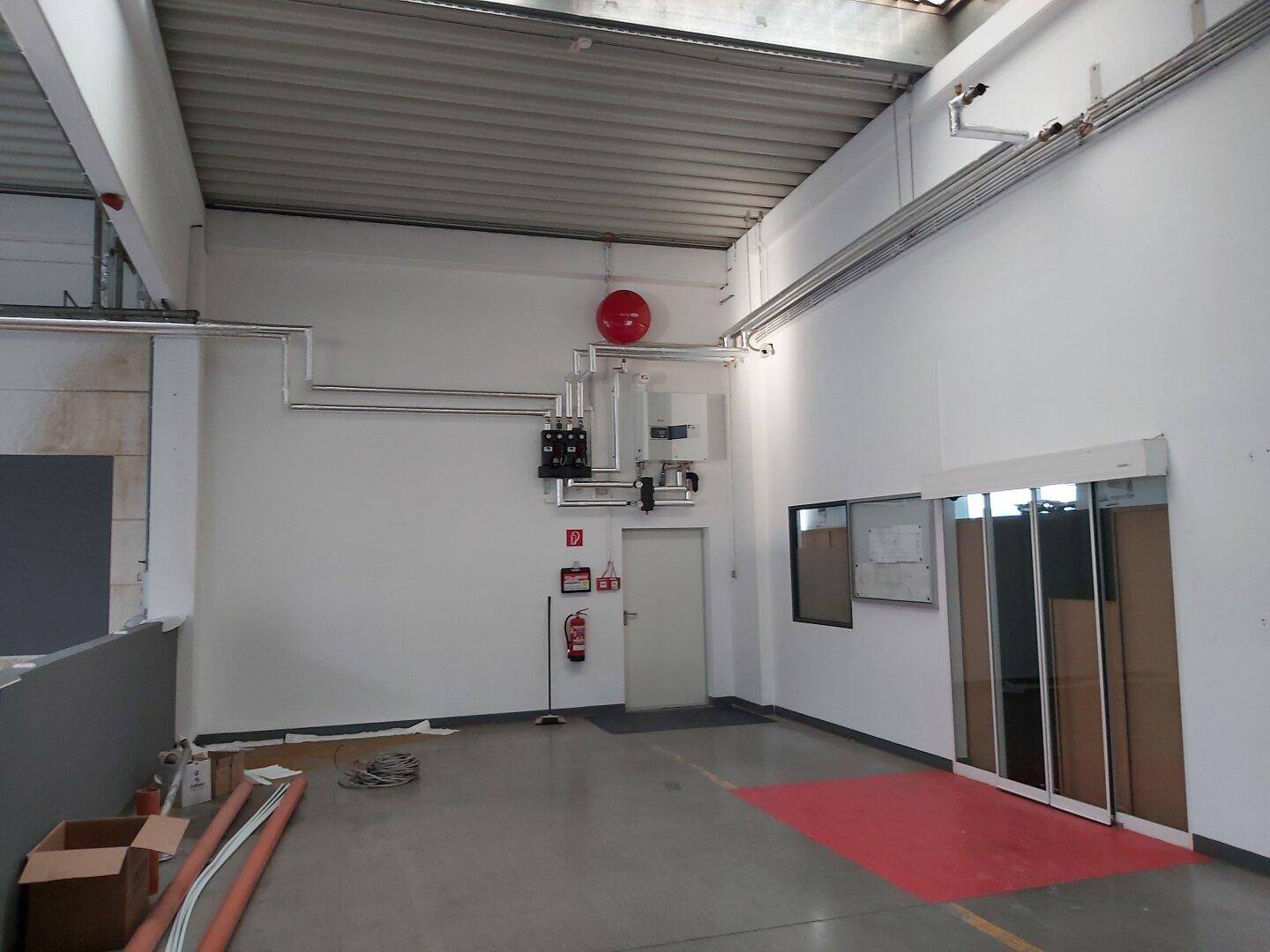 Ecke des Industrieraums mit sichtbaren Versorgungsleitungen, Brandschutzvorrichtungen und einer Glasschiebetür.