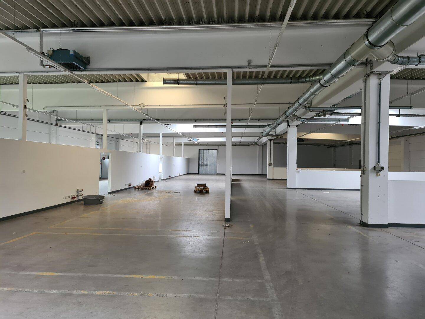 Weitläufiger leerer Industrieraum mit hohen Decken, Betonboden und funktionalen Trennwänden, bereit zur Nutzung.