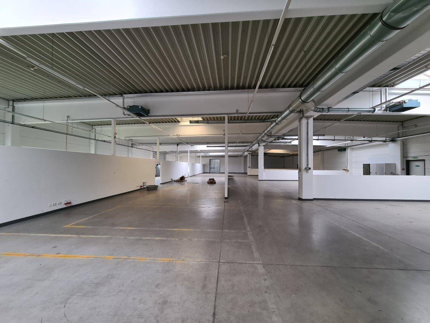 Weitläufiger Industrieraum mit Wellblechdecke, sichtbaren Lüftungsrohren und funktionalen Trennwänden.