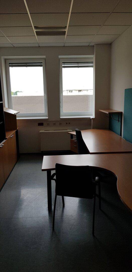 Kleines Büro mit zwei Fenstern, dunklem Boden und Holzmöbeln.