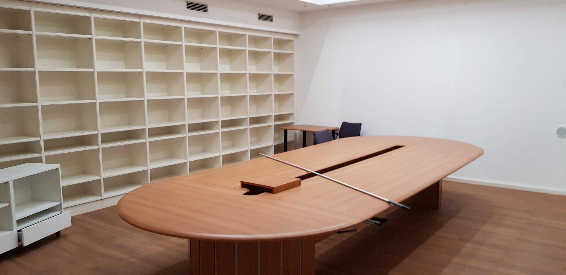Großer Konferenzraum mit ovalem Holztisch und einer Wand voller Regale.