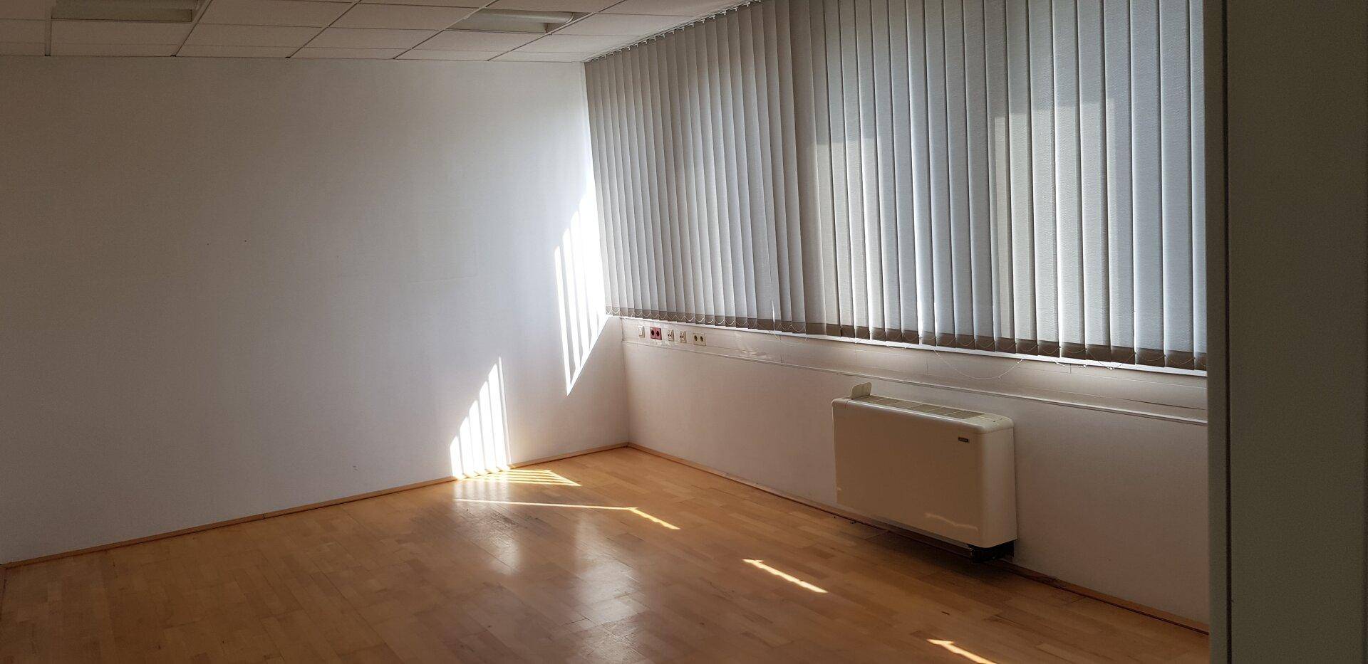 Leerer Büroraum mit Holzfußboden, vertikalen Jalousien und viel natürlichem Licht.