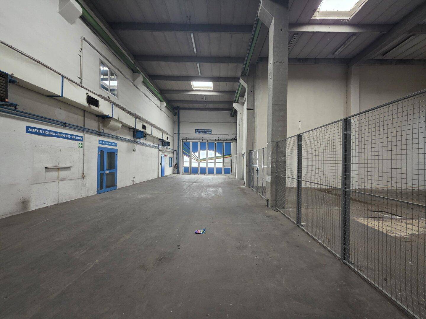 Industrielle Lagerhalle mit großem Rolltor, Betonboden und hohen Decken, bereit für den Warenumschlag.