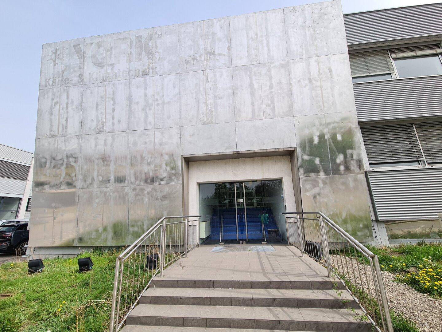 Eingangsbereich des Gebäudes mit breiter Treppe und einer strukturierten Fassade.