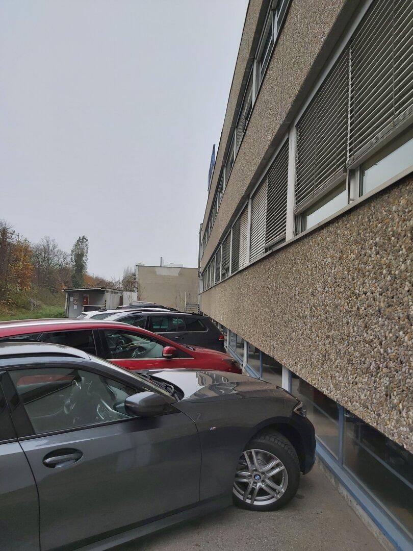 Seitenansicht des Gebäudes mit geparkten Autos und Fenstern mit Jalousien.