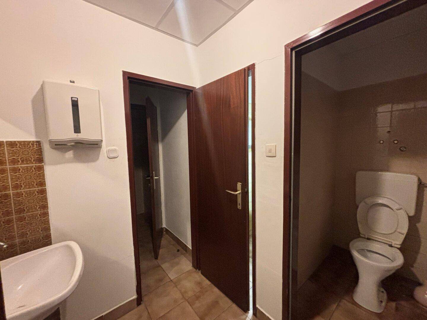 Toilettenbereich mit Waschbecken, WC und braunen Wandfliesen, in einfachem Zustand.