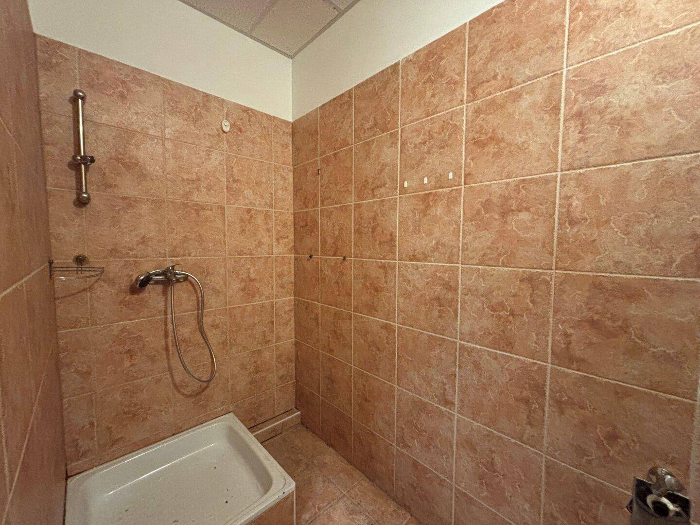 Gefliester Duschbereich mit braunen Wand- und Bodenfliesen, ausgestattet mit Duschkopf und kleiner Duschwanne.