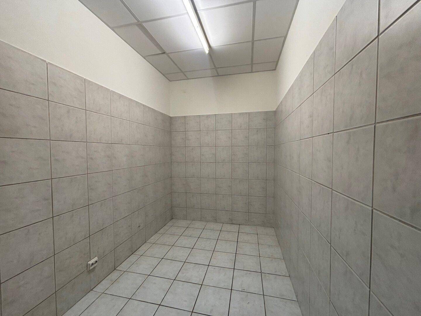 Kleiner Raum mit grauen Wand- und Bodenfliesen und einer abgehängten Decke mit Leuchtstoffbeleuchtung.