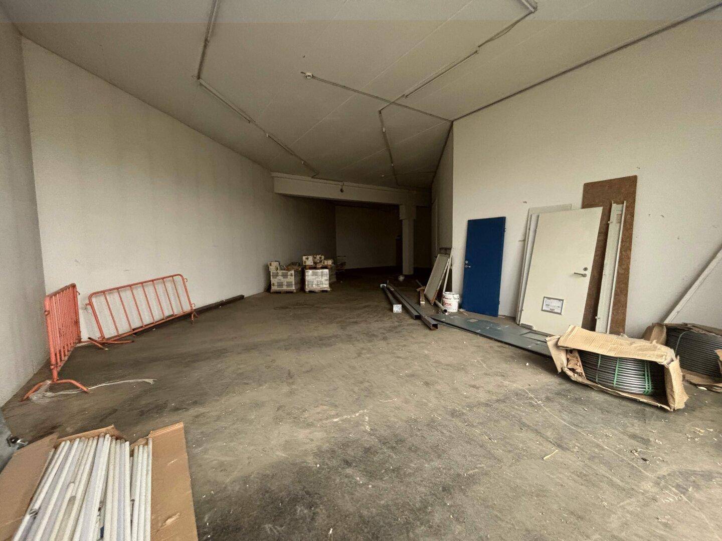 Großer, unmöblierter Gewerberaum mit Betonboden, Säulen und Baumaterialien, ideal für individuelle Gestaltung.