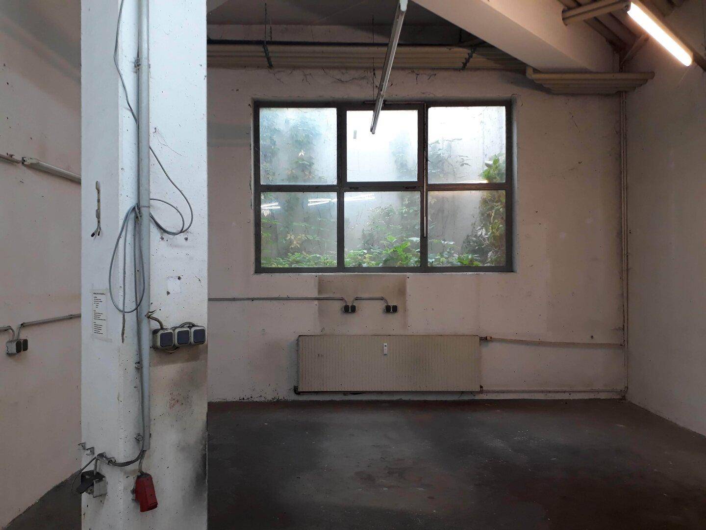 Fensterbereich in einem Gewerberaum mit Blick ins Grüne, Heizkörper und sichtbaren Elektroinstallationen.