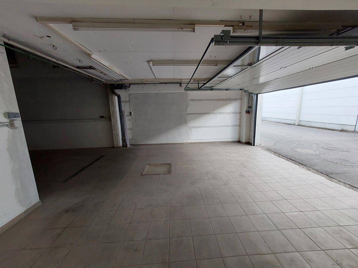 Geräumige Garage mit Fliesenboden und offenem Rolltor, das den Zugang zum Außenbereich ermöglicht.
