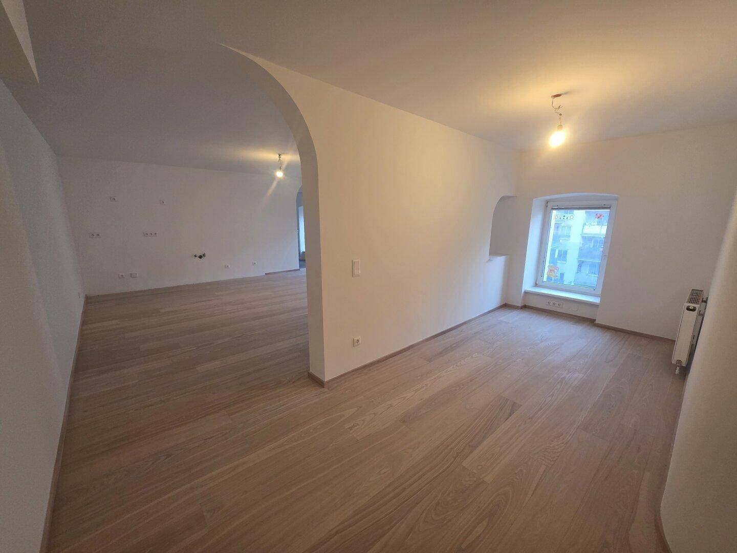 Großzügiger Wohnbereich mit hellem Holzparkett, der durch einen eleganten Bogen unterteilt ist.