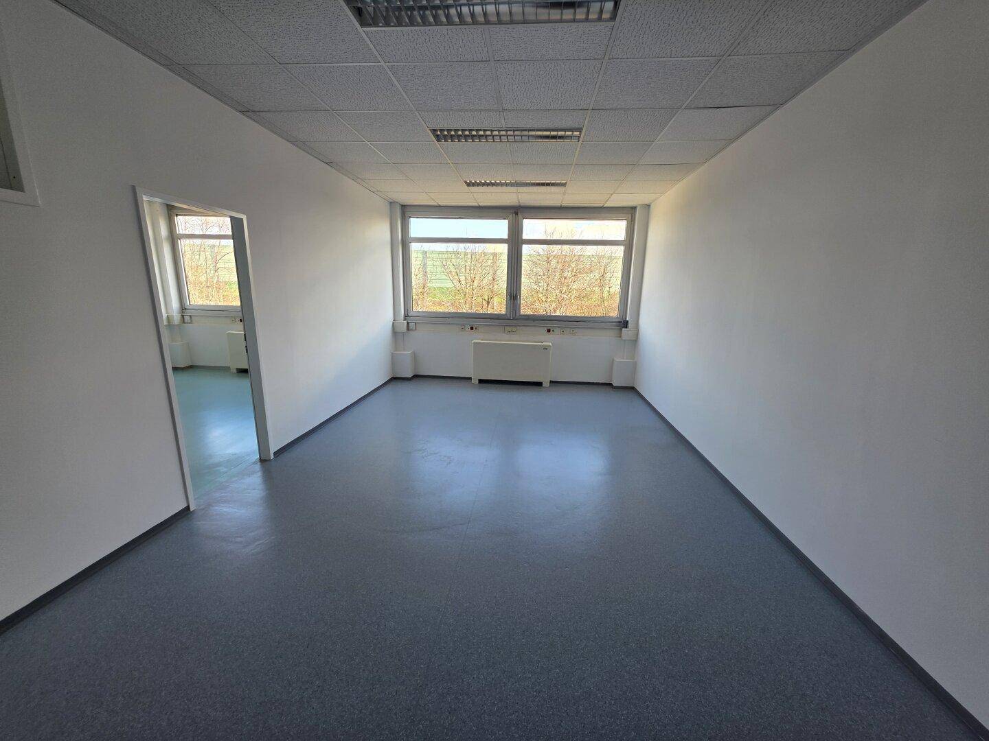 Geräumiges, leeres Büro mit großen Fenstern, die viel Tageslicht hereinlassen und einen weiten Blick bieten.