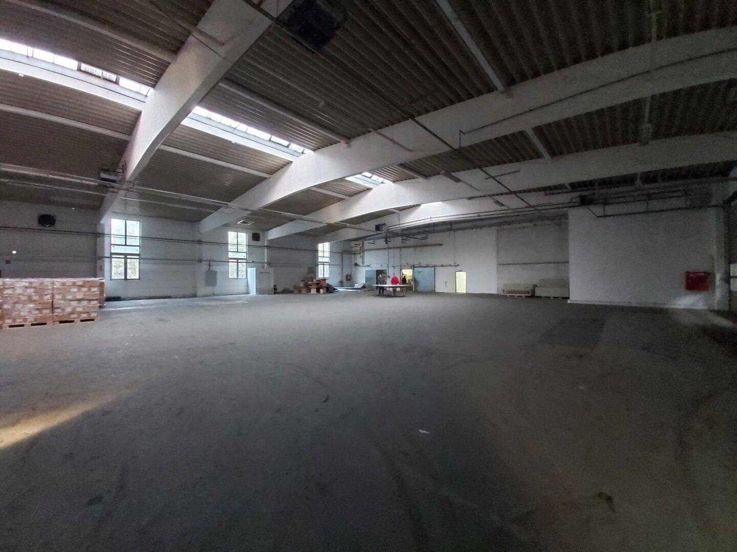 Weitläufige Lagerhalle mit hohen Decken, großen Fenstern und Oberlichtern, die viel natürliches Licht hereinlassen.