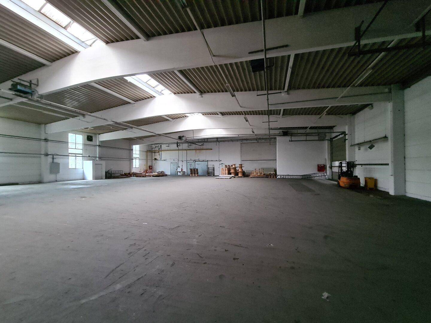 Weitläufige Lagerhalle mit Betonboden, hohen Decken und Oberlichtern, bereit für die Nutzung, mit einem Gabelstapler.