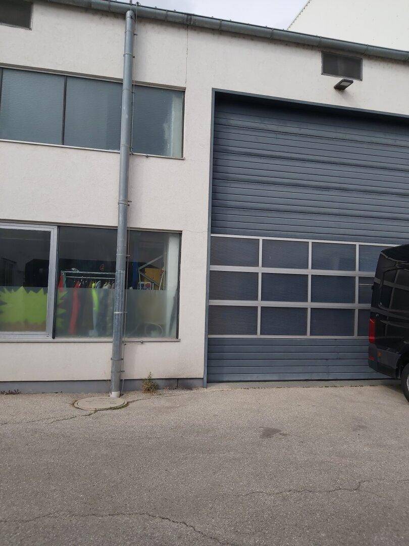 Weiße Industriefassade mit großem grauen Sektionaltor und Fenstern im Obergeschoss, daneben ein Lieferwagen.