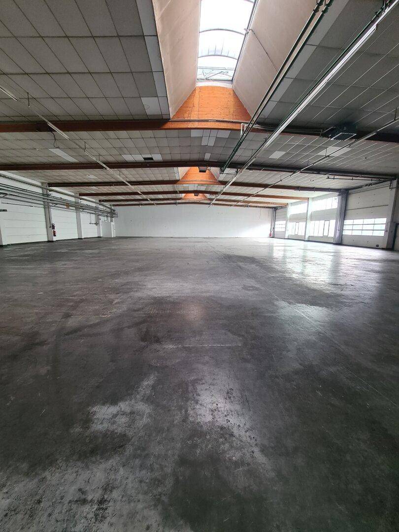 Geräumige, leere Industriehalle mit hohen Decken und großen Oberlichtern, die den gesamten Bereich erhellen.